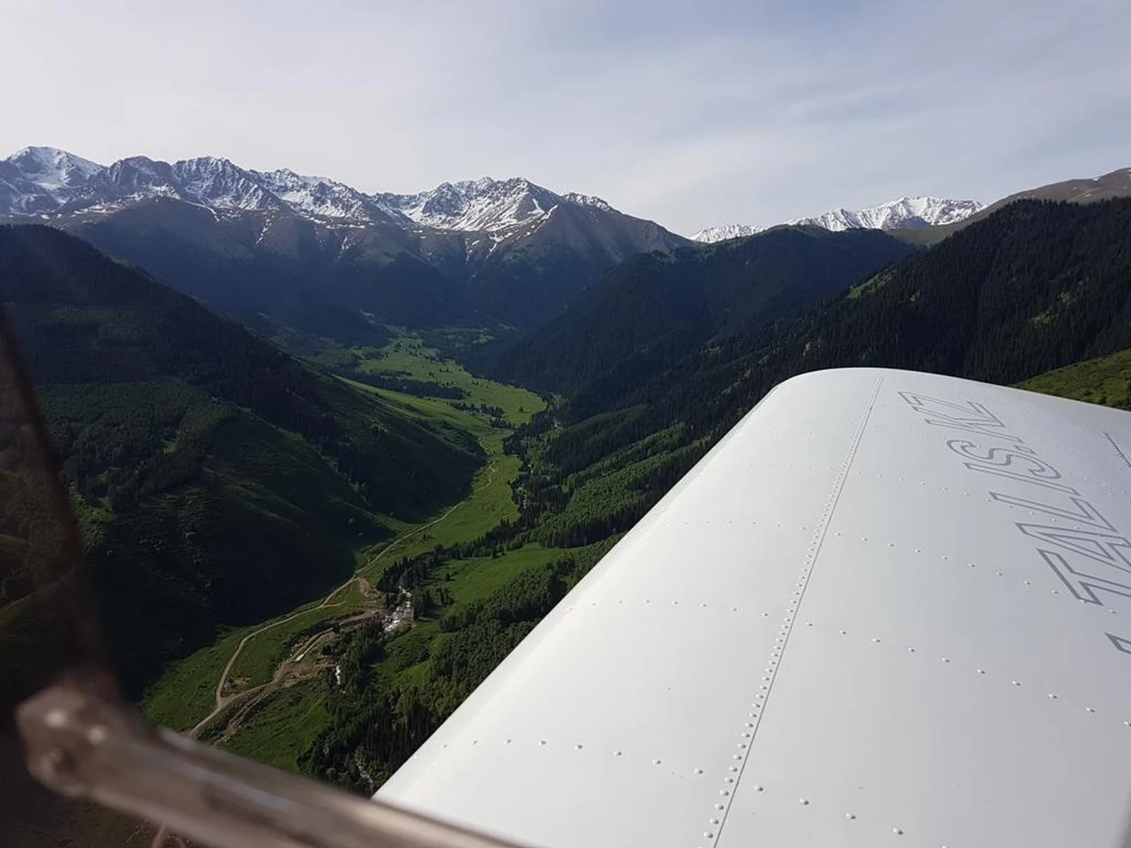 View of a green mountain valley and snow-capped peaks from a small plane's wing